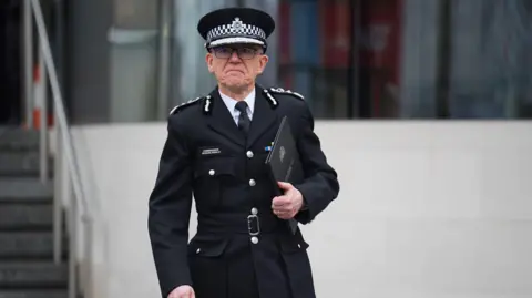 PA Media Sir Mark Rowley, in police uniform, holding a folder on the steps of New Scotland Yard