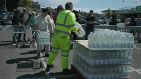 A queue of residents and a pallet of bottled water