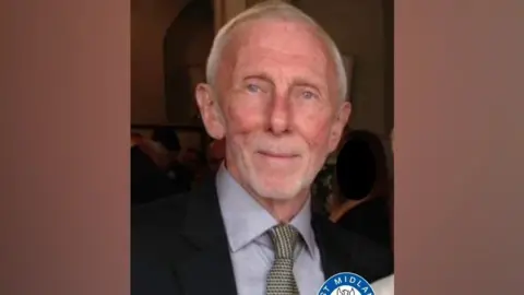 Michael Brady, a man with grey hair, is wearing a grey shirt and black suit jacket with a patterned tie.