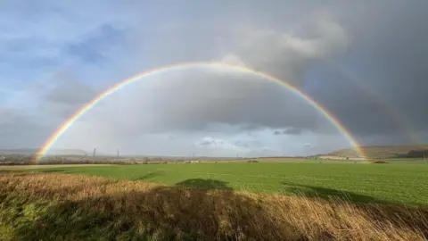 WeatherWatchers/Corvus A full rainbow seen stretching across the fields of Pewsey. A mild reflection, or a second rainbow, can be glimpsed above the one lower down.
