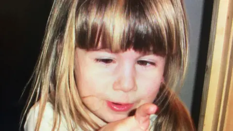 supplied A very young girl with long straight fair hair and a fringe holding up her hand to her face