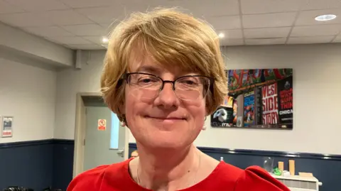 BBC/Grace Wood A woman with short blonde hair wearing a red dress