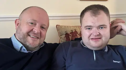 Tom sits next to his father Sid on a sofa