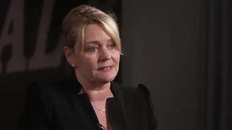 Sharon Graham in a black jacket against a dark background being interviewed by the BBC