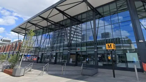 Google Streetview of Sunderland station. It is a large glass building. There is a black pole outside, atop of which stands a yellow cube with a large black M and the word Metro written on it.