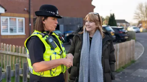Wiltshire Police A woman with a puffy jacket and large light blue scarf talking to a female police officer in uniform on a residential street
