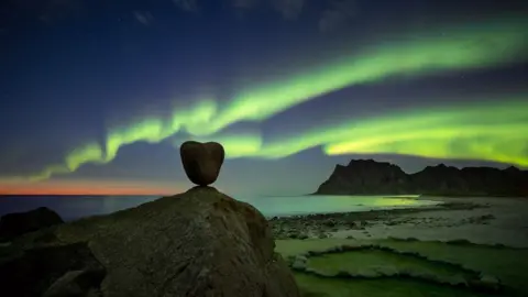 The aurora in the night sky behind a heart shaped rock