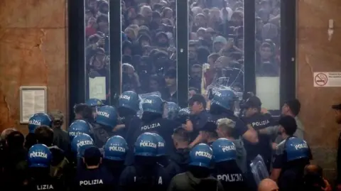 MOURAD BALTI TOUATI/EPA/Shutterstock Protesters outside a window clash with police inside the window wearing blue helmets at Milan's Central Station during a pro-Palestinian protest