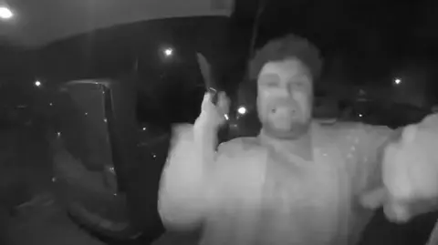 Cumbria Police Black and white footage from a doorbell camera showing Daniel Lytollis about to strike the equipment with a knife. He is slightly blurred through motion and has gritted teeth,