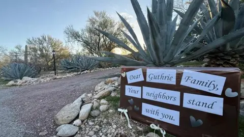 Neighbours have erected signs for the Guthrie family. The sign under a cactus says, "Dear Guthrie Family Your neighbors stand with you."