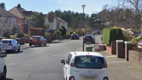 A street view of Lynton Road. There are cars lining the street and there and houses with red brick walls in front of their garden.