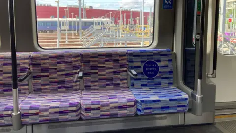 A blue patterned priority seat next to purple patterned seats on a Tube train.
