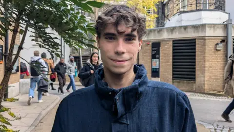 Dylan with brownish  hair, lasting  successful  a street, wearing a overgarment  and smiling