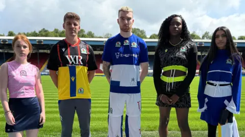 Five models - three women and two men on Blackburn Rovers' pitch at Ewood Park wearing recycled football kits.