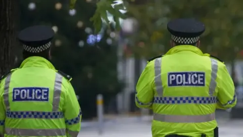 PA Media Image shows two police officers patrolling Liverpool City Centre. They are wearing hi-vis jackets and are photographed from behind. 