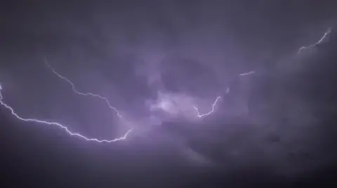 Weather Watchers/Narnia A lightning bolt in the sky in Wiltshire. The sky is purple toned from the flash.