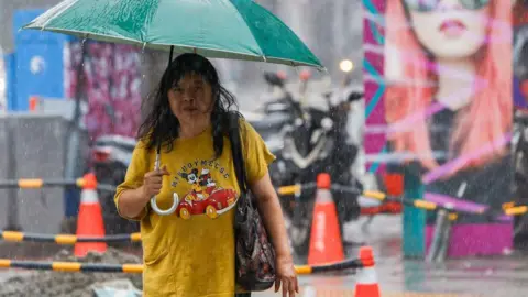 Getty Images A woman walks in the rain as Typhoon Gaemi is rapidly approaching the island, in New Taipei, Taiwan