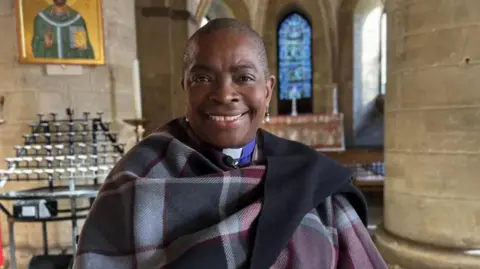 BBC Close up image of a smiling Rose Hudson-Wilkin Bishop of Dover inside a church.