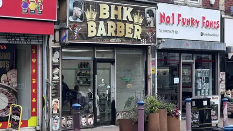 BHK Barber shop front on a highstreet. The barber shop is part of a rank of shops. 