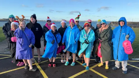 Burr Point Buoys A group of winter swimmers wearing colourful hats and robes, gathered and smiling outdoors.