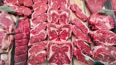 Raw steaks are lined up on a counter at a grocery store.