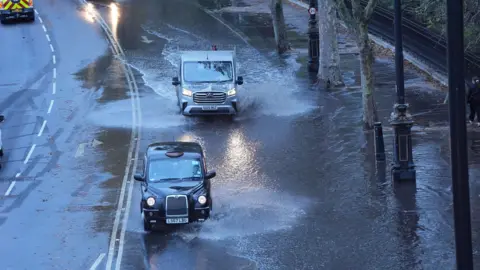 PA Media A black cab and a van driving through floodwater in Victoria Embankment in central London