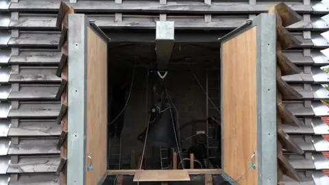 A black bell inside the top of the church tower. Filmed using a drone.