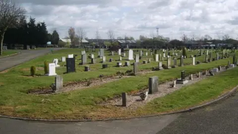 Nuneaton and Bedworth Borough Council A plot of land in a cemetery. Rows of graves are visible on an area of green grass, surrounded by a circular road.