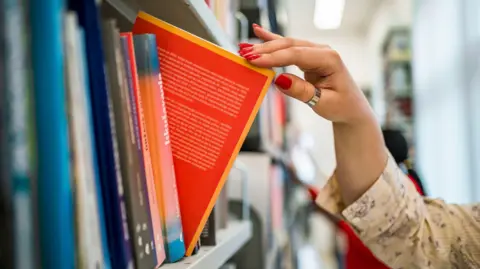Woman's hand picking a book from a library bookshelf - stock photo