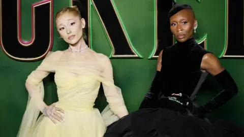 EPA-EFE/REX/Shutterstock Ariana Grande (left) and Cynthia Erivo (right) on the green carpet at the UK premiere of Wicked at the Royal Festival Hall in London, on 18 November 2024. 