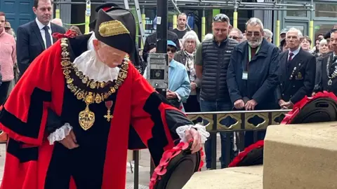 Newbury Town Council Newbury's mayor in his ceremonial red robes laying a wreath as onlookers gather in the background