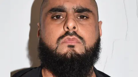 Close up of Man with shaven hair and dark beard in black clothing