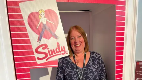 Melissa Barnett in a doorway surrounded by carboard cut to look like a pink Sindy box