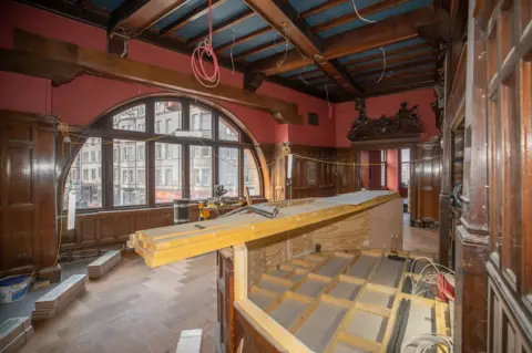 Mike Hume A huge room with red walls and original wooden features, with a half constructed bar and a half circle window looking out onto Home Street in Edinburgh 