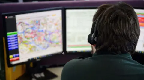 An emergency services call handler sitting at a desk with a headset on taking a call