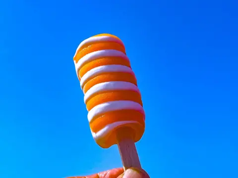 Orange and white lolly held up against bright blue sky