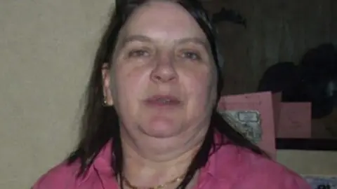 A woman with long brown hair wearing a pink shirt