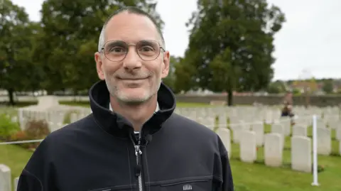 Dr Stephan Naji looking at the camera with war graves behind him