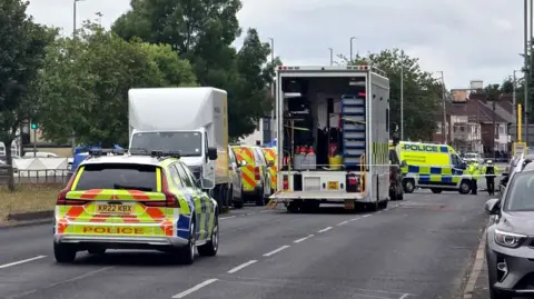 A number of police vehicles close off dual carriageway in Merseyside. The road has trees lined down the middle