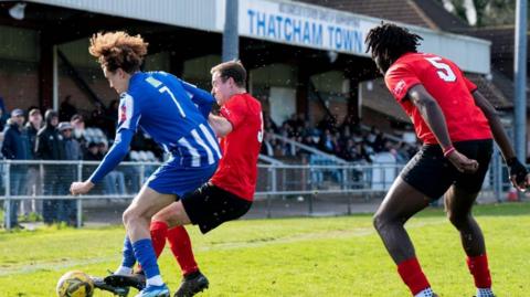 A Thatcham player - white, with curly hair - is challenged by an opposition player - white with dark hair - at Thatcham Town's Waterside Park ground 