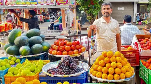 Arun Kumar Arun Kumar se encuentra en su puesto de frutas con pilas ordenadas de melones, granadas, uvas y más.