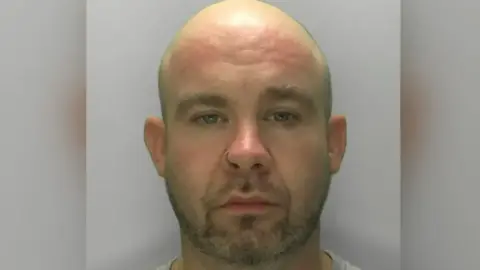 Gloucestershire Constabulary A custody mugshot of Kane Kotwica. He has a shaved head and light stubble