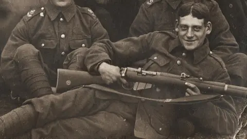 Percy Walsh lies in front of his comrades, smiling and holding a gun and wearing full military uniform