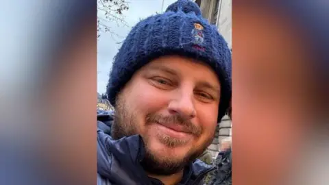 Handout image featuring an informal shot of Daniel Loft, who is wearing a bobble hat and smiling at the camera