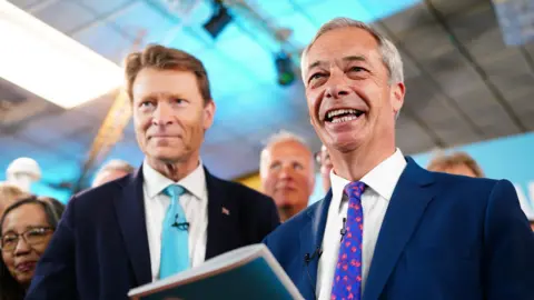 Reform UK chairman Richard Tice and party leader Nigel Farage are seen smiling at a campaign event in 2024.