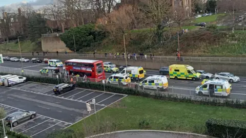 Wide amateur shot of the stationary bus after the attack, surrounded by emergency vehicles
