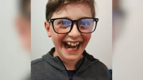 Family handout Kyle Sieniawski, laughing. Kyle has a huge smile, large black-rimmed glasses and wears a grey hooded top.