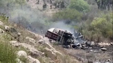 Reuters The remains of a vehicle surrounded by smoke at the bottom of a rocky hill
