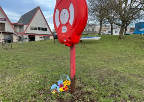 Flowers on grass near a boat club, after discovery of bodies