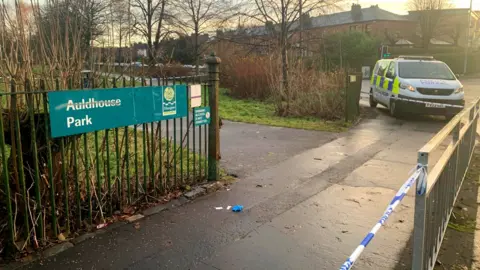 BBC The gated entryway of Auldhouse park with police tape and a Police Scotland van parked on the pavement